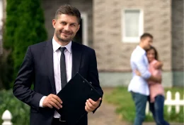 Man standing with clip board and couple hugging behind him