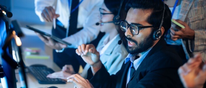 customer support agent wearing a headset works at a computer while teammates coordinate nearby in a busy call center, representing bpo services.