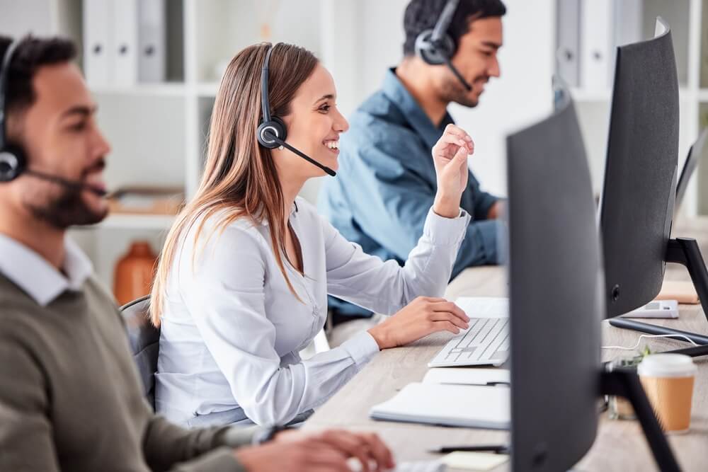 Call center agents wearing headsets assist customers from computer stations, showing the value of a reliable call center services provider.