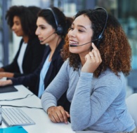 Customer service call center team of agents wearing headsets, assisting customers at computers in a modern office environment.