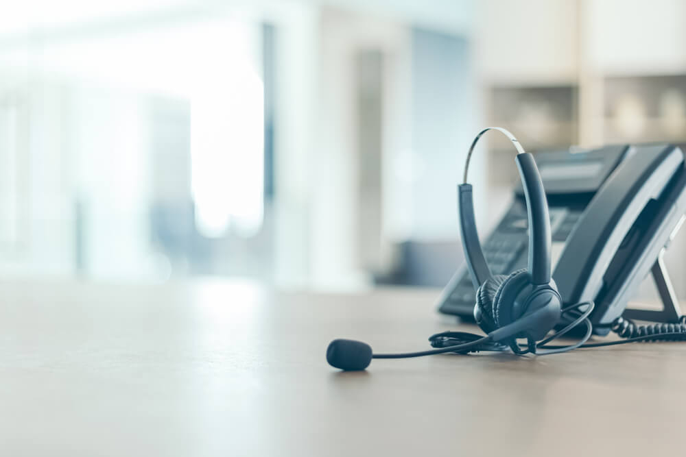 Customer service call center headset resting on a desk next to office telephones in a modern workspace, representing customer support and call center operations.