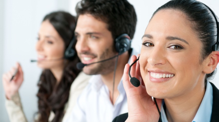Three nearshore BPO workers in a call center with closest one smiling at camera.