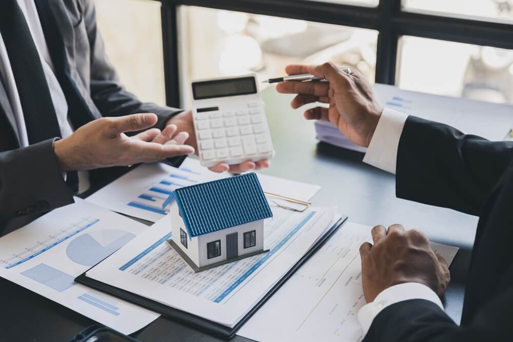 Hands of real estate sales professionals hold calculator and go over big data to improve results.