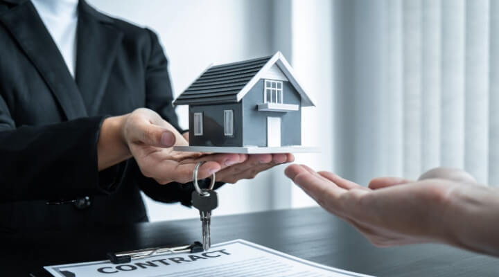 Real estate agent handing over a model home and keys above a signed contract, showing how bpo helps real estate firms streamline property transactions and client support.