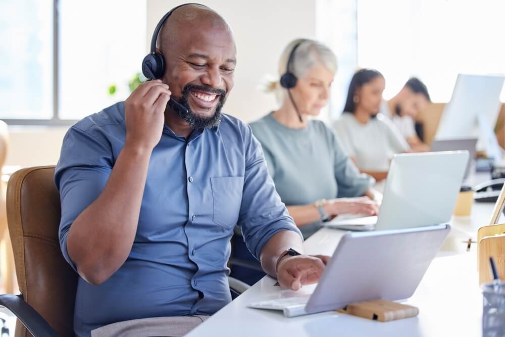 Black man, laptop and call center agent smile or sales consultant or customer service worker for inbound support in the office. Happy male pc operator or outbound or telemarketing.