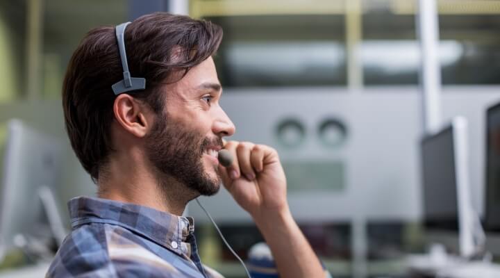 Smiling male customer service representative talking on headset to help with end-of-year outsourcing cost savings.