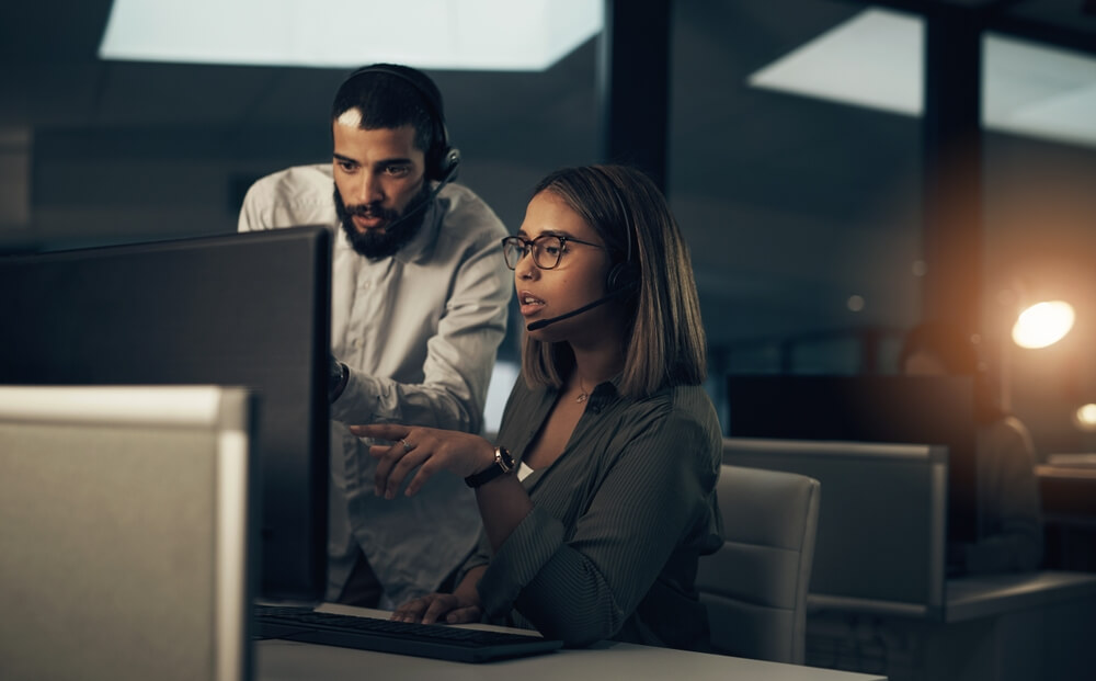Night, call center and man with woman on computer for 24/7 holiday customer support outsourcing, customer service, CRM support and telemarketing.