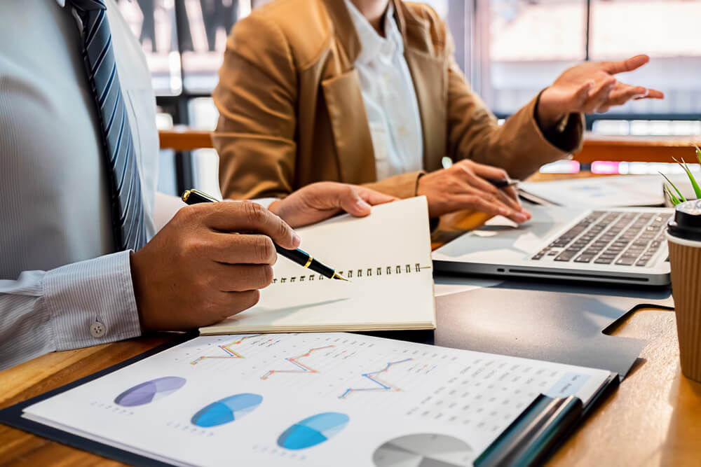 Expert in a suit and an entrepreneur review accounts at a table covered with growth diagrams, planning to outsource small business bookkeeping.