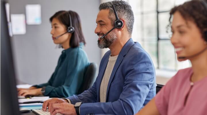 Group of call center agents, two women and one man, working efficiently and smiling during their calls, demonstrating BPO cost reduction.