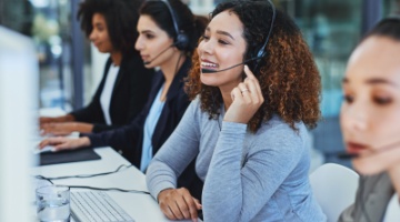 Customer service call center team of agents wearing headsets, assisting customers at computers in a modern office environment.