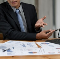 Business meeting discussing BPO contract with professional presenting charts and graphs on a tablet, with reports on the table.