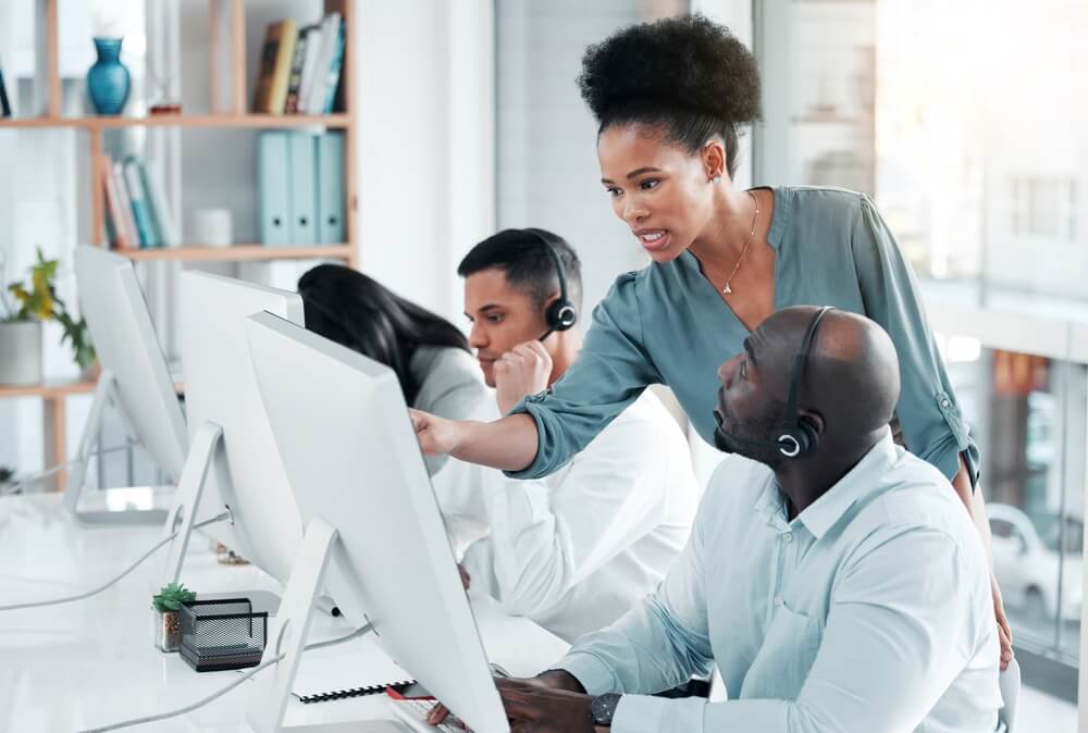 Team lead coaching headset-wearing agents at computer workstations in a bright office, supporting Back-Office BPO Services.