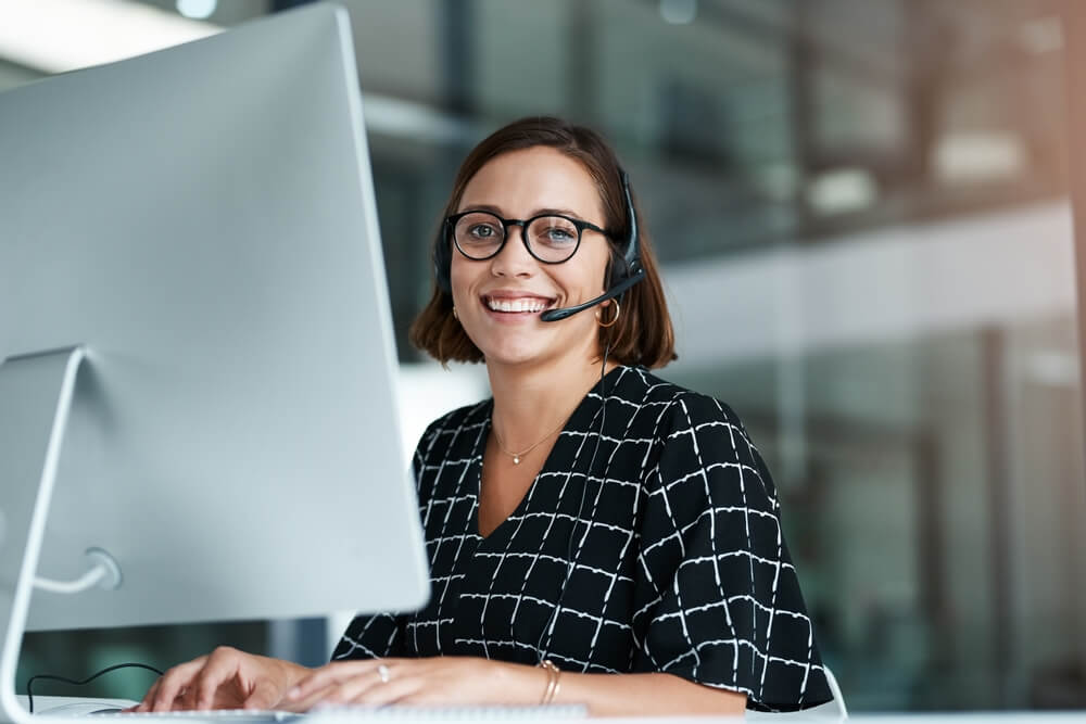 Customer support agent smiling at her desk, representing successful outsourcing and professional client service.
