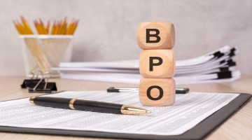 BPO business concept with wooden blocks spelling BPO on office paperwork beside a pen, pencils, and stacked documents.