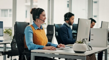 Agents working at computers in a modern BPO customer service center, wearing headsets and assisting customers.