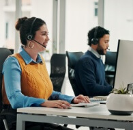 Agents working at computers in a modern BPO customer service center, wearing headsets and assisting customers.