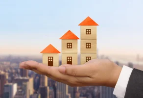 Real estate agent holding three house models on his hand in a city´s background.