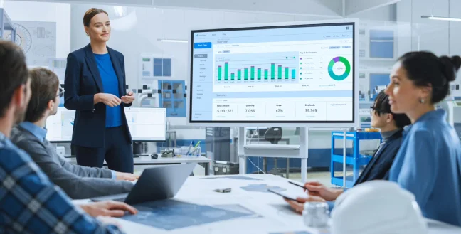 A woman in a conference explaining charts on the screen to her coworkers.