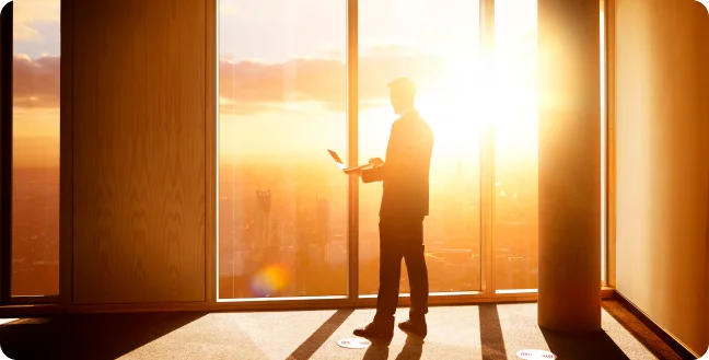 Silouette of a bussinesman against window with city sunset