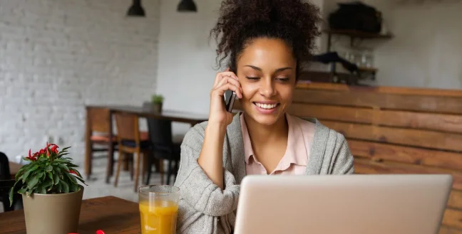 African American woman calling by phone and using a laptop in a cafeteria.